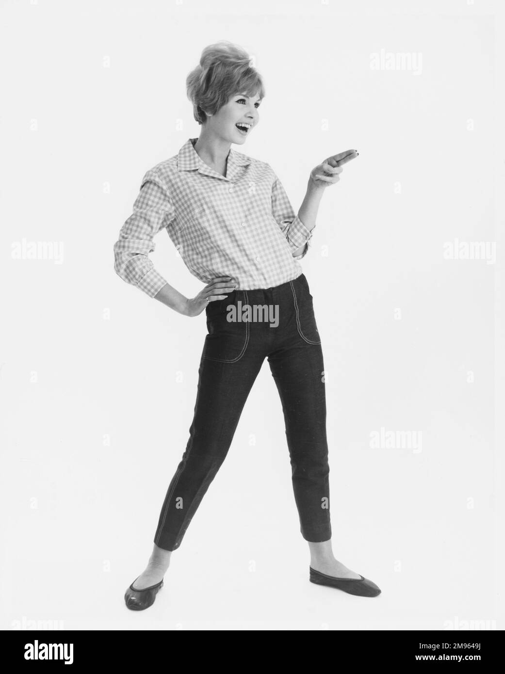 Ritratto a tutta lunghezza di un modello in una camicia a scopata e jeans corti posa con le dita facendo una pistola. Foto Stock