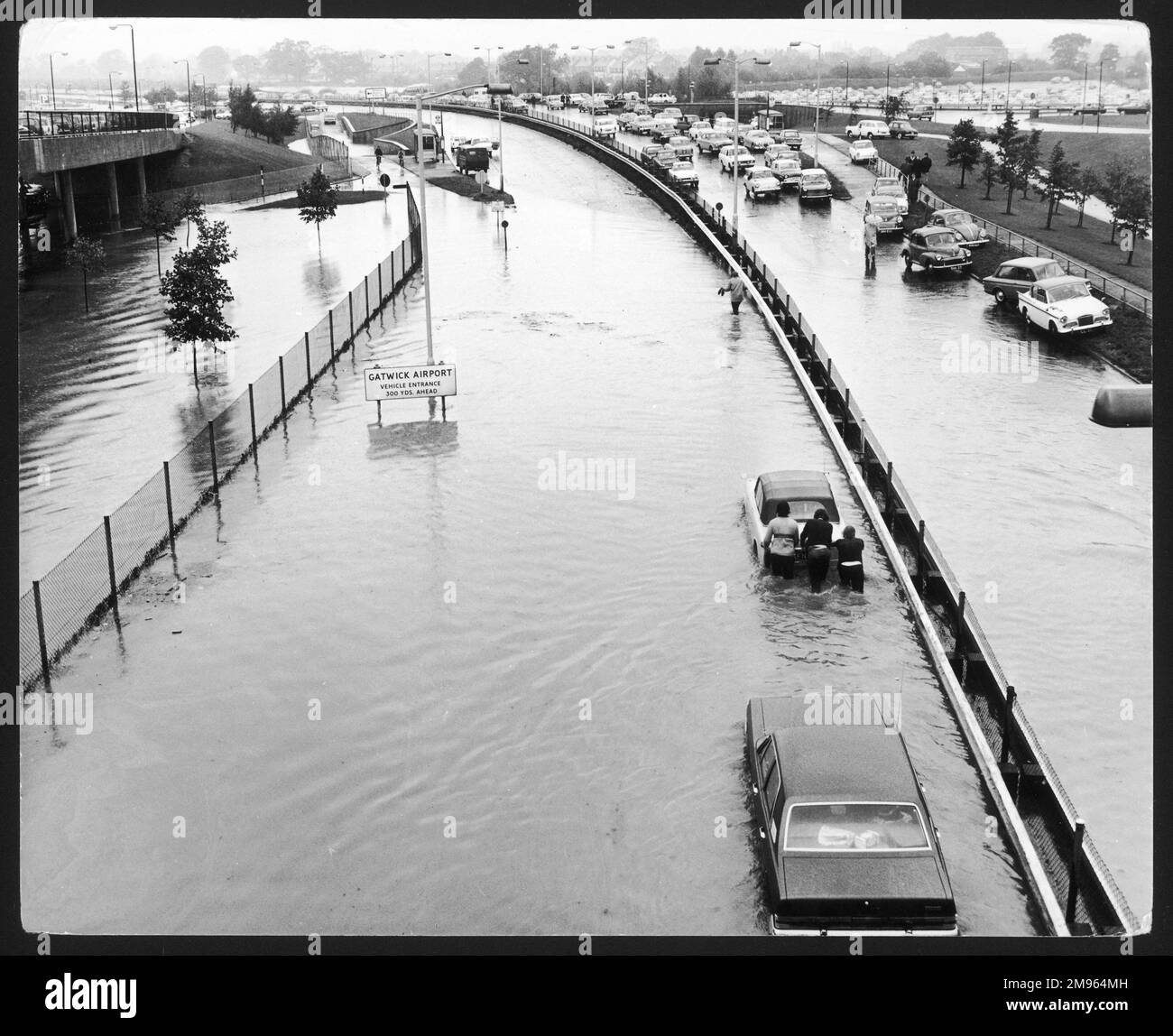 Una scena incredibile, come qualcosa di un film di disastro, come la gente svanisce attraverso le inondazioni, spingendo le loro auto lungo la strada A23 fuori dall'aeroporto di Gatwick, Inghilterra. Foto Stock