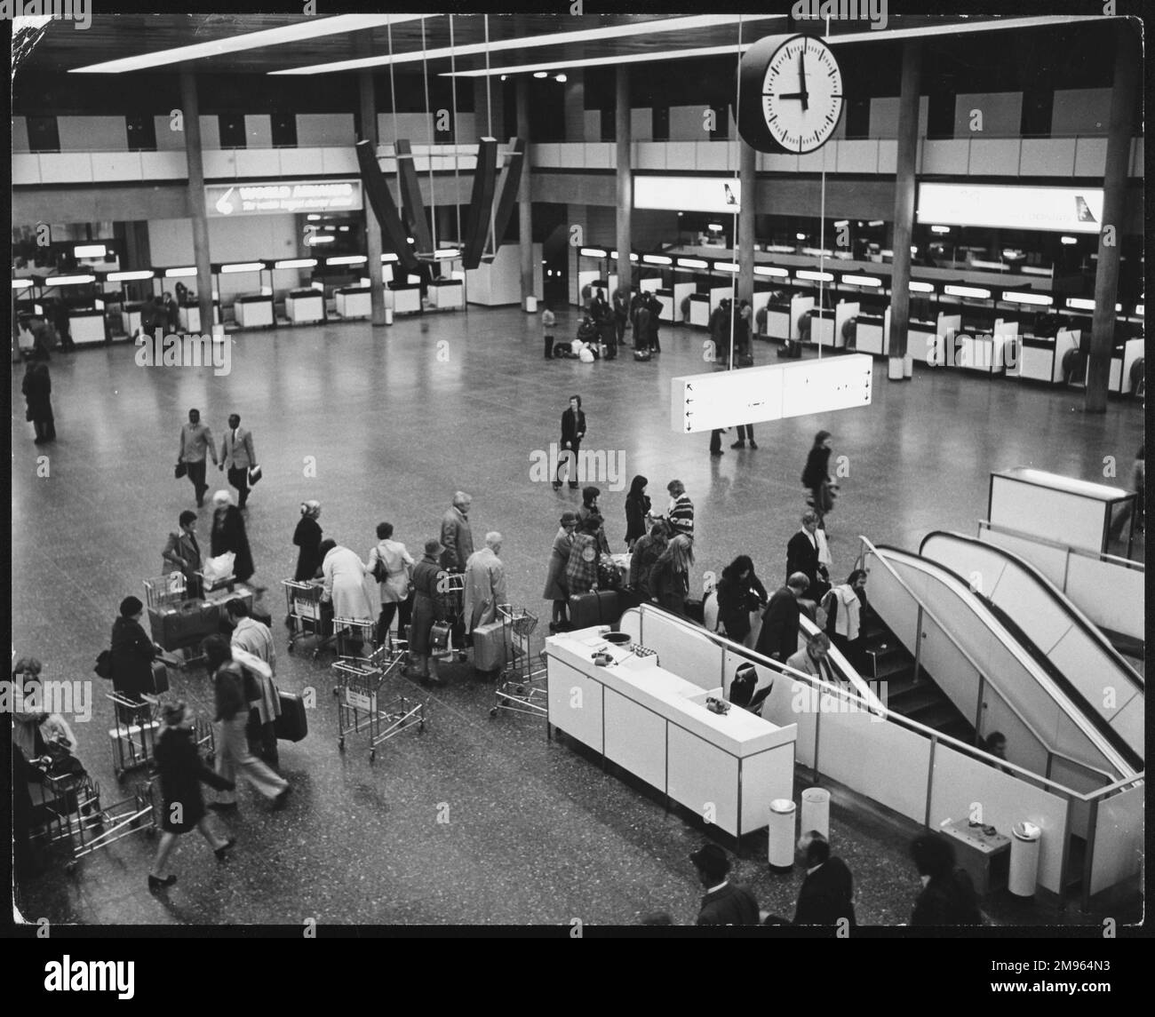 L'interno dell'aeroporto Gatwick di Londra, mostrando ai passeggeri che spingono i bagagli sui carrelli verso la parte superiore delle scale mobili. Foto Stock