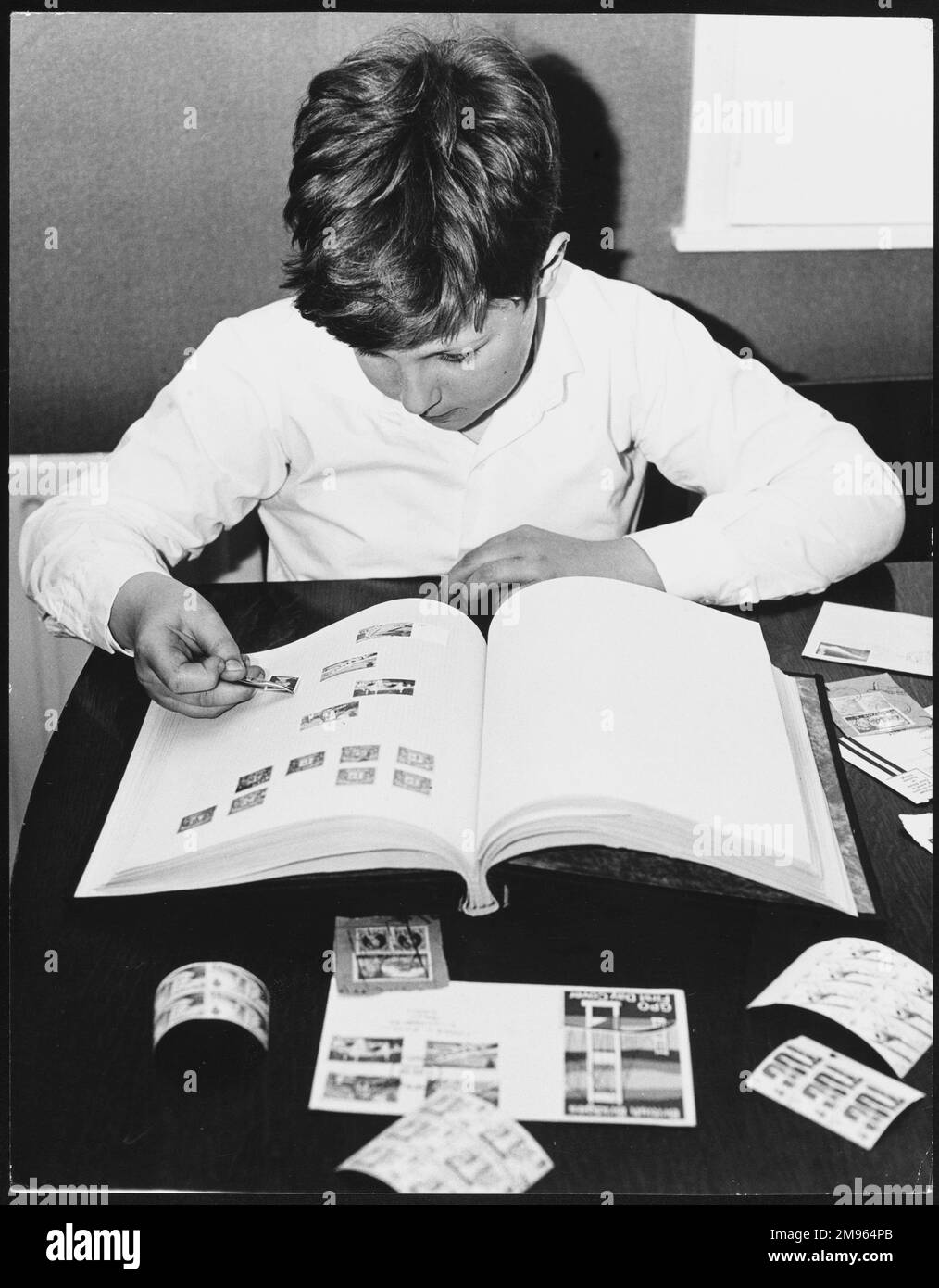 Un collezionista di francobolli ragazzo, attaccando francobolli nel suo libro di francobolli Foto Stock