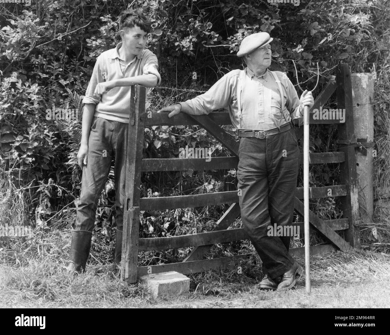 Due lavoratori agricoli posano appoggiandosi su un cancello. Foto Stock
