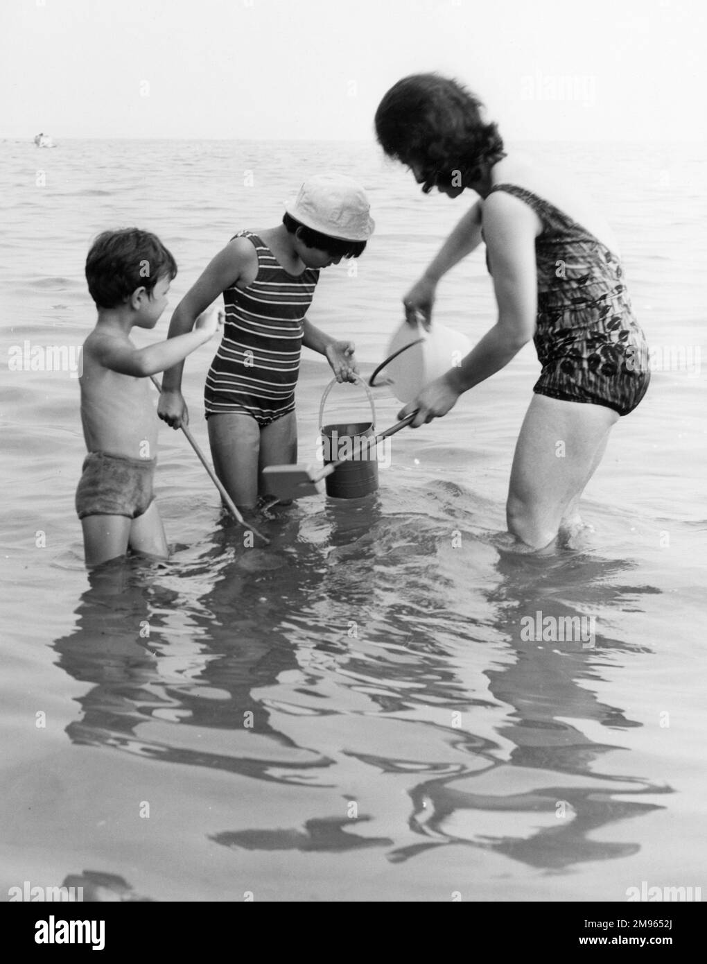 Una famiglia cerca di trovare le cose in mare con i loro secchi e reti. Foto Stock