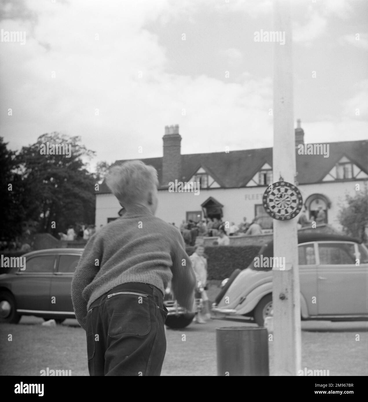 Un giovane ragazzo che gioca a freccette, la sua tavola inchiodata a un palo all'aperto, fuori dalla flotta (Arms?) Pub, Worcestershire. Fotografia di Norman Synge Waller Budd Foto Stock