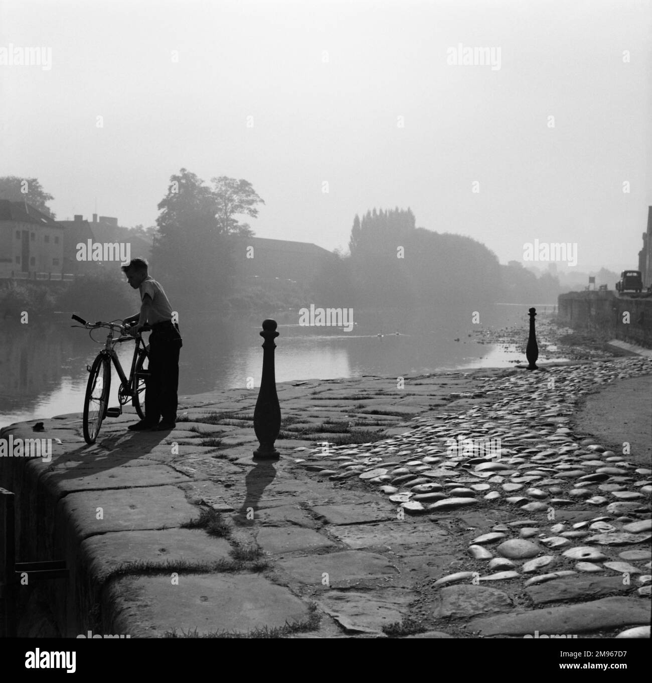 Un ragazzo e la sua bicicletta sulle rive del fiume Severn a Bewdley Bridge, Worcestershire. Fotografia di Norman Synge Waller Budd Foto Stock