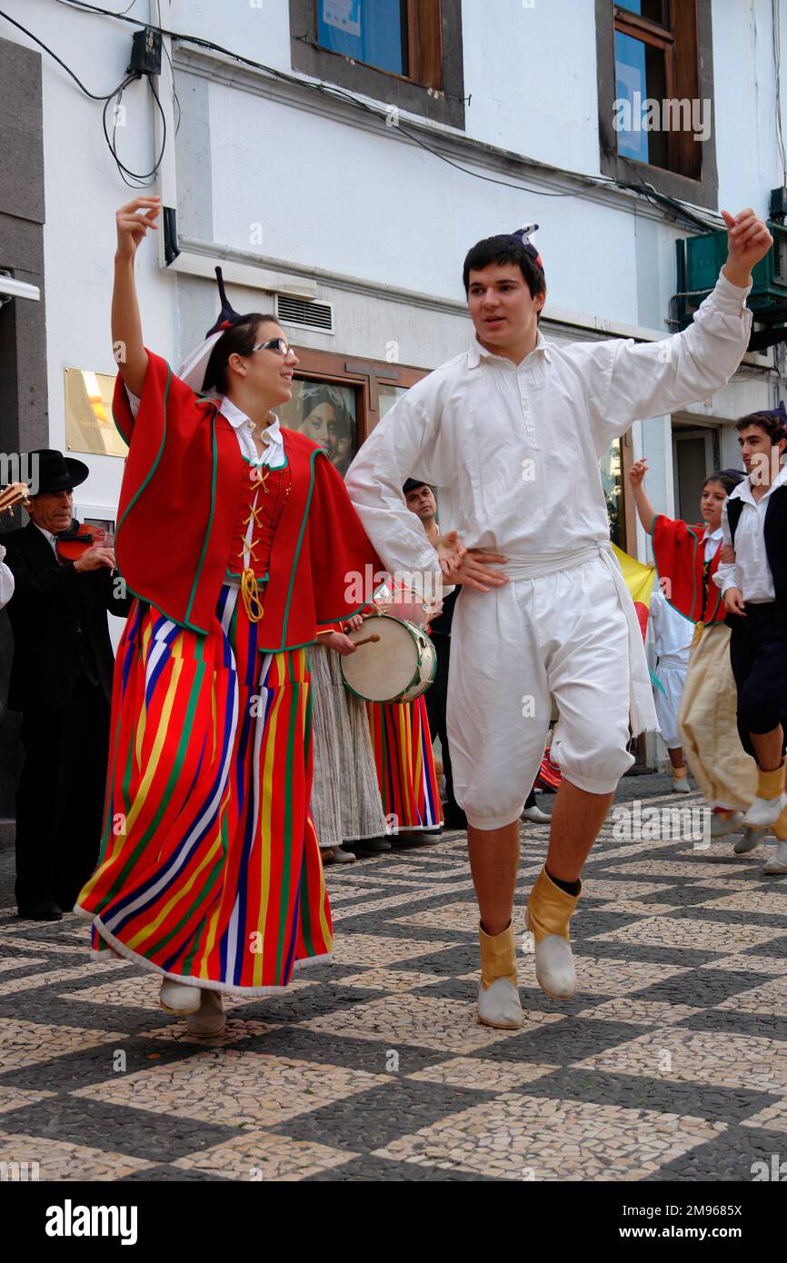 Due membri di un gruppo folcloristico di Gaula, visto qui ballare a Funchal, la capitale di Madeira, con musicisti che suonano sullo sfondo. La coppia indossa un costume tradizionale, compresi i cappucci neri del cranio con punte. La donna indossa prevalentemente rosso, compresa una gonna a righe lunghe. L'uomo è vestito di bianco. Foto Stock