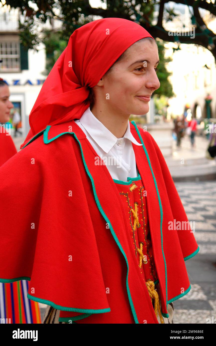 Una giovane donna di un gruppo folcloristico gaula, che indossa un costume tradizionale, composto da un mantello rosso brillante, un abito e un velo. Si trova a Funchal, la capitale di Madeira, partecipando al divertimento di strada. Foto Stock