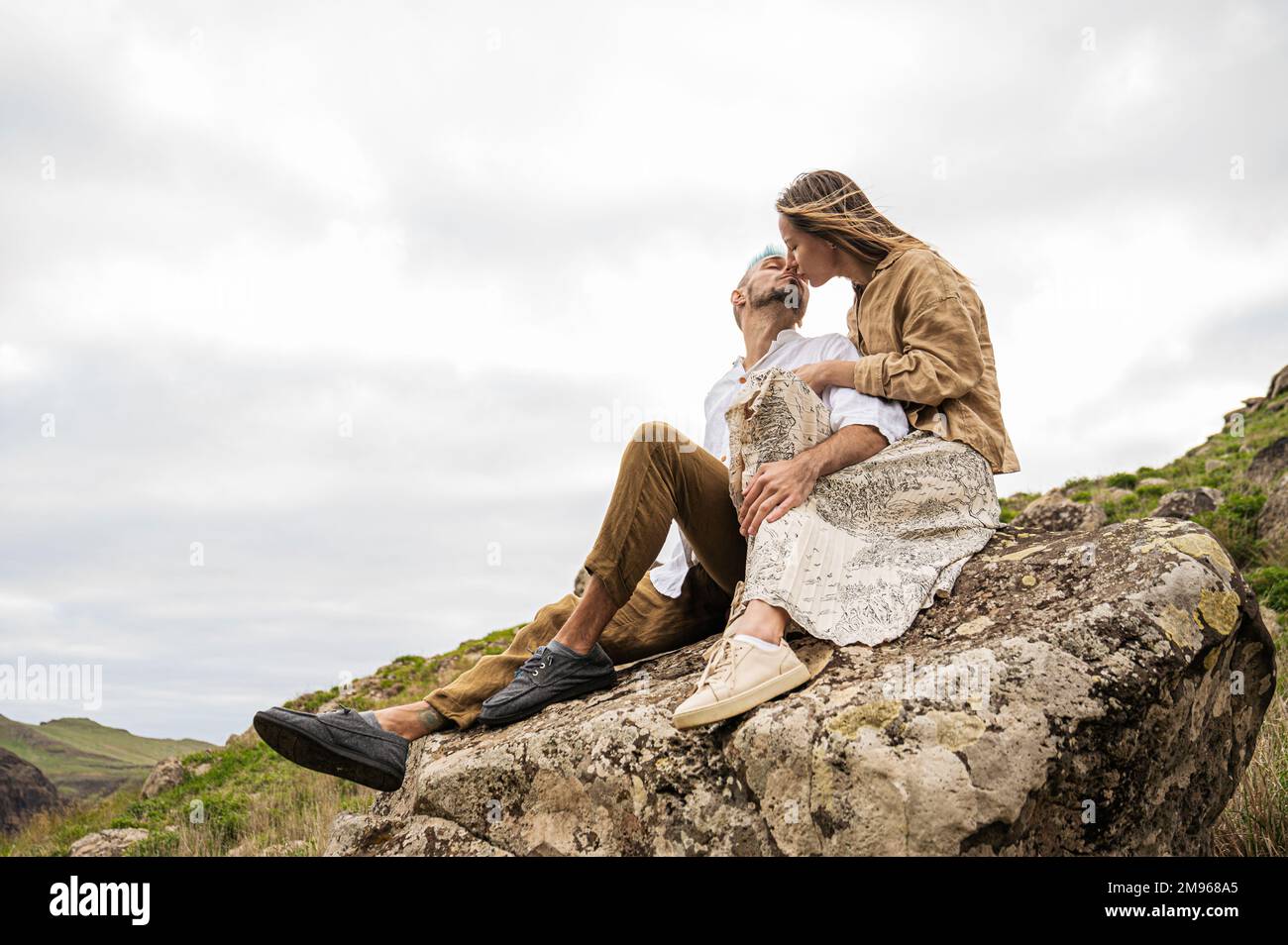 Una giovane coppia bacia su una roccia circondata da colline e rocce sullo sfondo Foto Stock