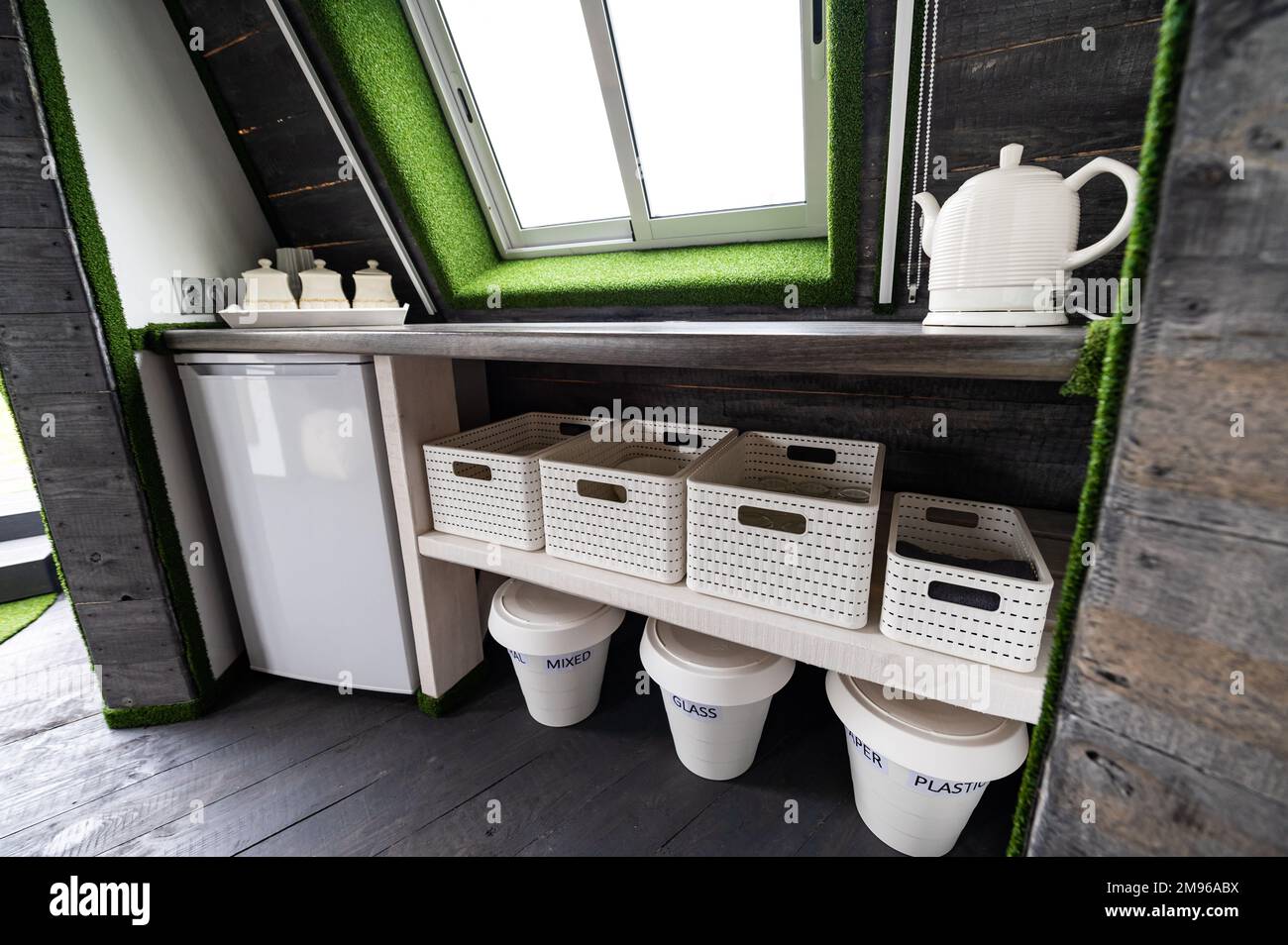 Piccoli elementi da cucina in casa estiva in legno. Frigorifero, bollitore, bevande calde, stoviglie e lattine di riciclaggio in piccola cucina. Originale, insolito, in Foto Stock