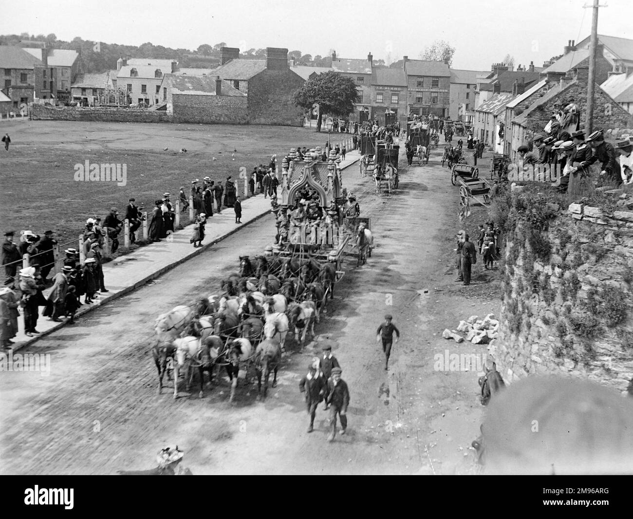 Street scene, che mostrano parte della parata del Circus di Sanger durante una visita a Haverfordwest, Pembrokeshire, Dyfed, Galles del Sud, con diverse elaborate carrozze trainate da cavalli e cavalieri vestiti con costumi di fantasia. La gente sui marciapiedi si ferma e guarda, e pochi ragazzi seguono sulla strada. Alcune persone sono sedute in cima ad un vecchio calefornio coperto da erba (a destra). Sanger fu un famoso impresario del circo, che a partire dagli anni '1850s organizzò spettacoli spettacolari in grandi locali in tutto il paese. Foto Stock