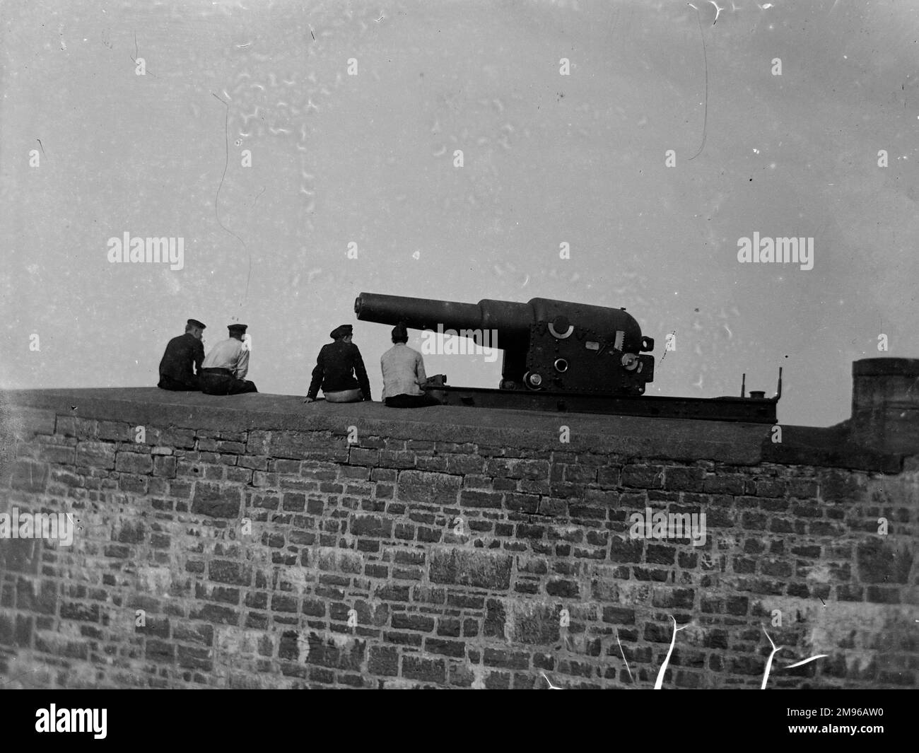 Un cannone Palliser a Stack Rock Fort, su una piccola isola al largo di Milford Haven, Pembrokeshire, Galles occidentale. Quattro uomini si siedono sul muro, rilassandosi. Il cannone di Palliser era rivoluzionario nel suo tempo, come era caricato muso, che garantiva una maggiore stabilità in volo e scopo. Foto Stock