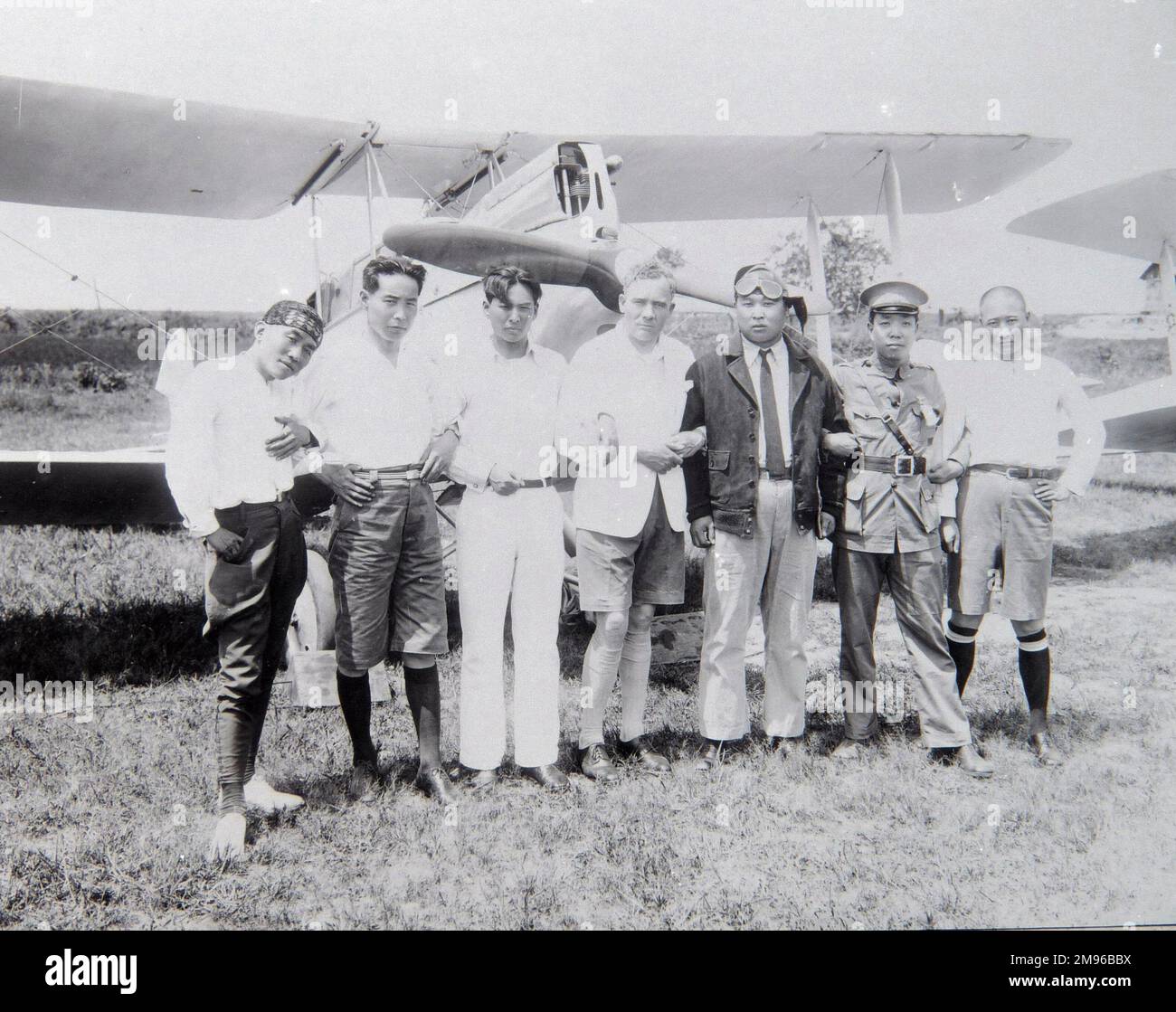 Aviatore occidentale in un viaggio in Estremo Oriente, in un campo con i suoi ospiti, in posa per la loro foto di fronte al velivolo. Foto Stock