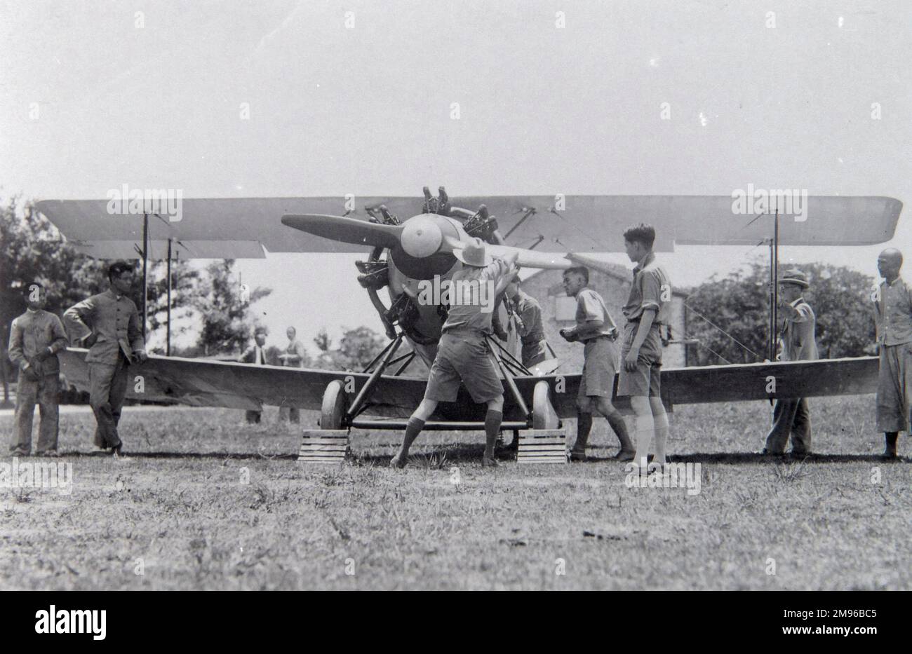 Uomini occidentali in un viaggio in Estremo Oriente, in un campo con i loro padroni di casa, cercando di far iniziare un aereo girando l'elica. Foto Stock