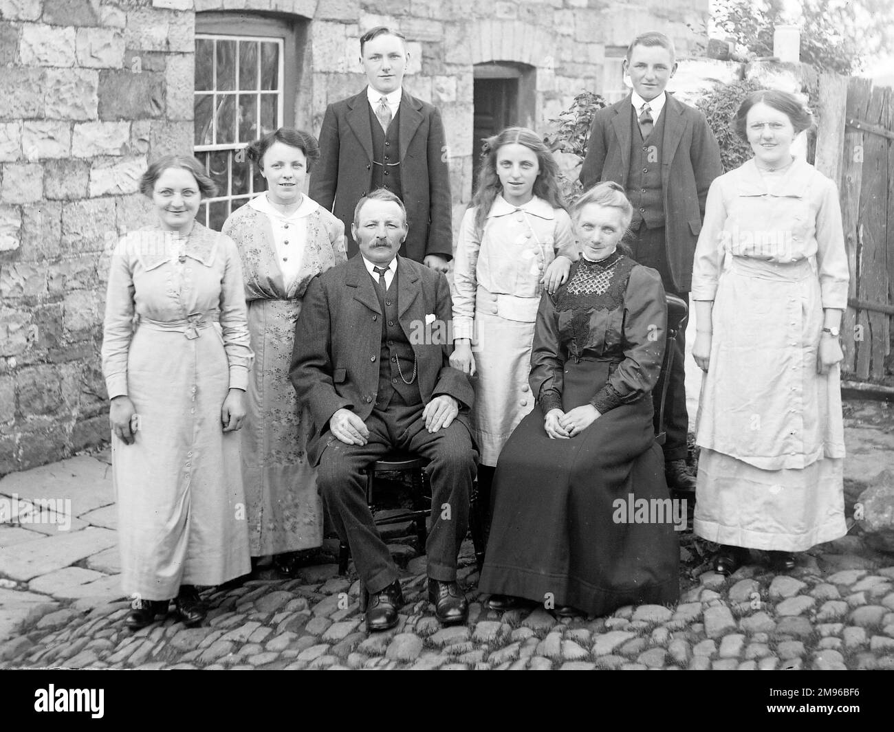 Una famiglia (cinque donne e tre uomini) posa per una fotografia di gruppo in un cortile acciottolato fuori una casa, probabilmente nella zona del Galles centrale. Foto Stock