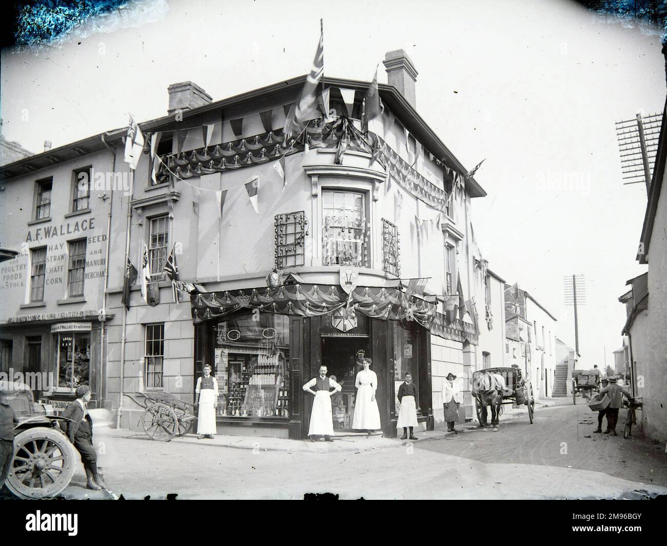 Una scena di strada con negozi, a Crickhowell, Powys, Galles centrale. Il grande negozio d'angolo è il negozio di alimentari Bell, decorato con bandiere, forse per celebrare l'Empire Day (24 maggio). Accanto ad esso sulla sinistra è AF Wallace, che vendono alimenti per animali e pollame, fieno, paglia, pula, mais, seme, concime, e frutta. Foto Stock