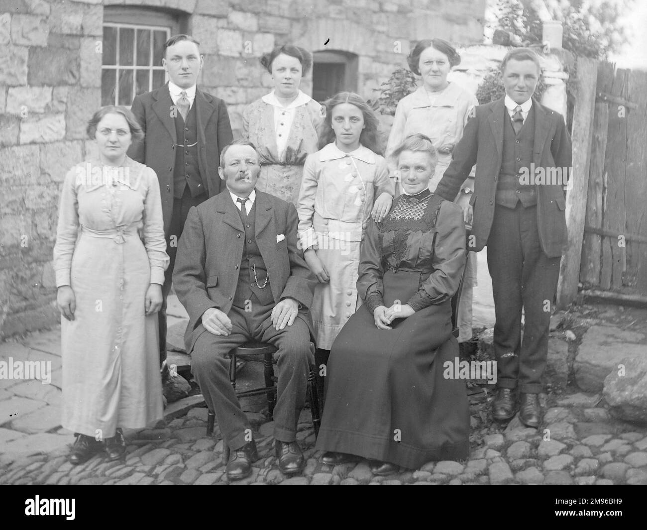 Una famiglia (cinque donne e tre uomini) posa per una fotografia di gruppo in un cortile acciottolato fuori una casa, probabilmente nella zona del Galles centrale. Foto Stock