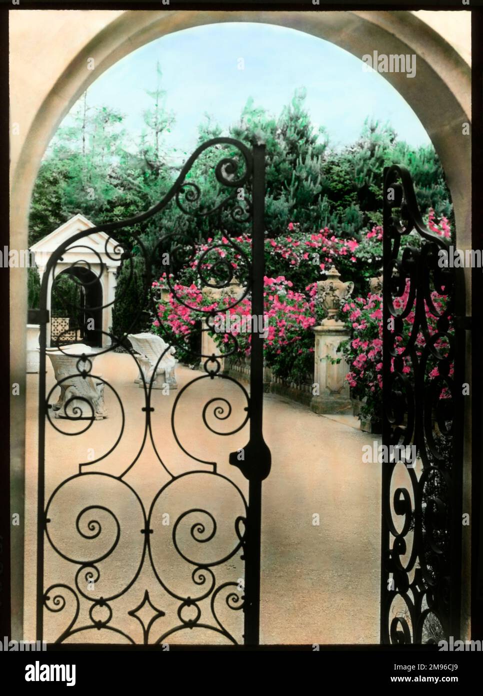 Vista sui giardini Compton Acres nel villaggio di Canford Cliffs, vicino a Poole, Dorset. Fiori rosa luminosi possono essere visti attraverso un arco con un cancello di ferro battuto. Foto Stock