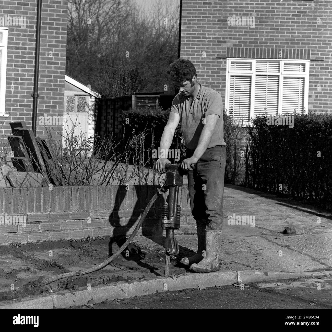 Un operatore utilizza un trapano pneumatico per scavare la pavimentazione. Foto Stock