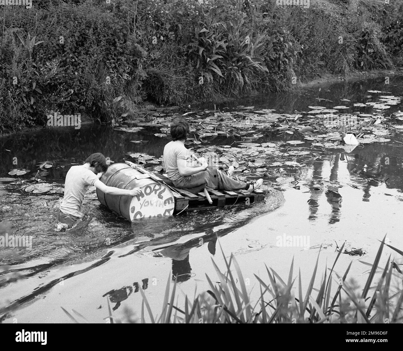 Due ragazzi con una zattera fatta di doghe di legno e un tamburo d'olio fanno la loro strada lungo un fiume. Sul tamburo sono dipinte le parole: Horley Youth Club. Foto Stock