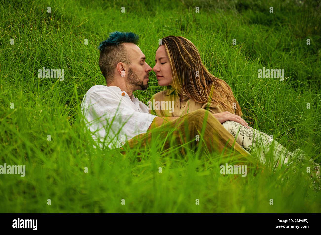 Una giovane coppia bacia in un campo di erba verde lussureggiante. Foto Stock