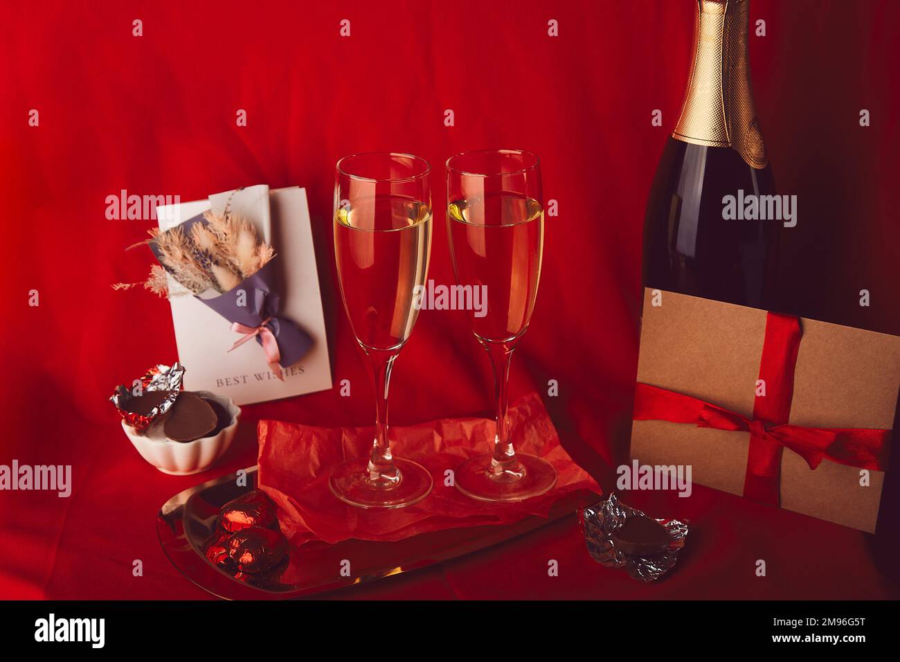 Tradizionale e romantica giornata di San Valentino con cartolina, champagne e regalo di carta su sfondo rosso. Foto Stock