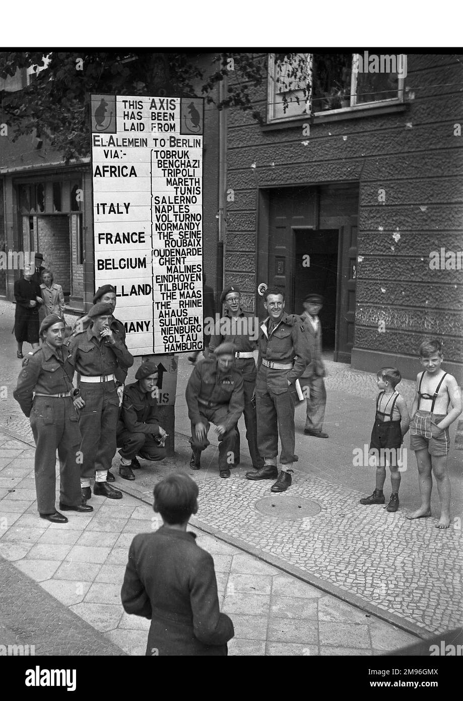 Street scene a Berlino, Germania, alla fine della seconda guerra mondiale, con soldati e bambini. Un segno recita: Questo asse è stato posato da El Alamein a Berlino via Africa, Italia, Francia, Belgio, Olanda, Germania, con vari nomi di località elencati. Foto Stock