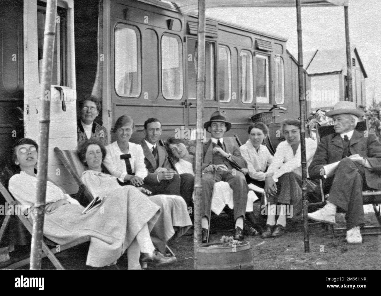 Un grande gruppo di vacanzieri seduti di fronte ad una carovana che sembra essere stata adattata da una vecchia carrozza ferroviaria. Foto Stock