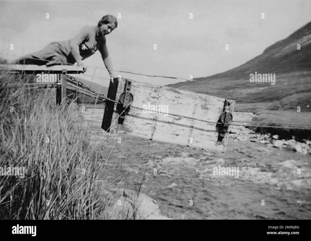 Una donna che spinge un traghetto box sospeso da corde attraverso un fiume. Foto Stock