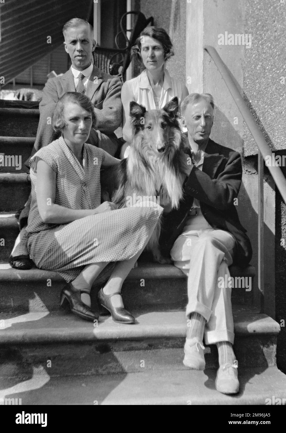 Quattro persone (due uomini e due donne) seduti sui gradini con un cane collie. Foto Stock