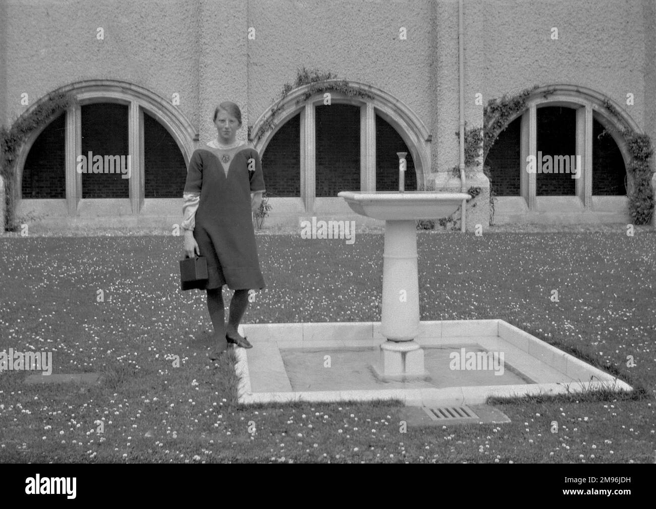 Una giovane donna in piedi accanto ad una fontana nel mezzo di un prato pieno di margherite. Foto Stock