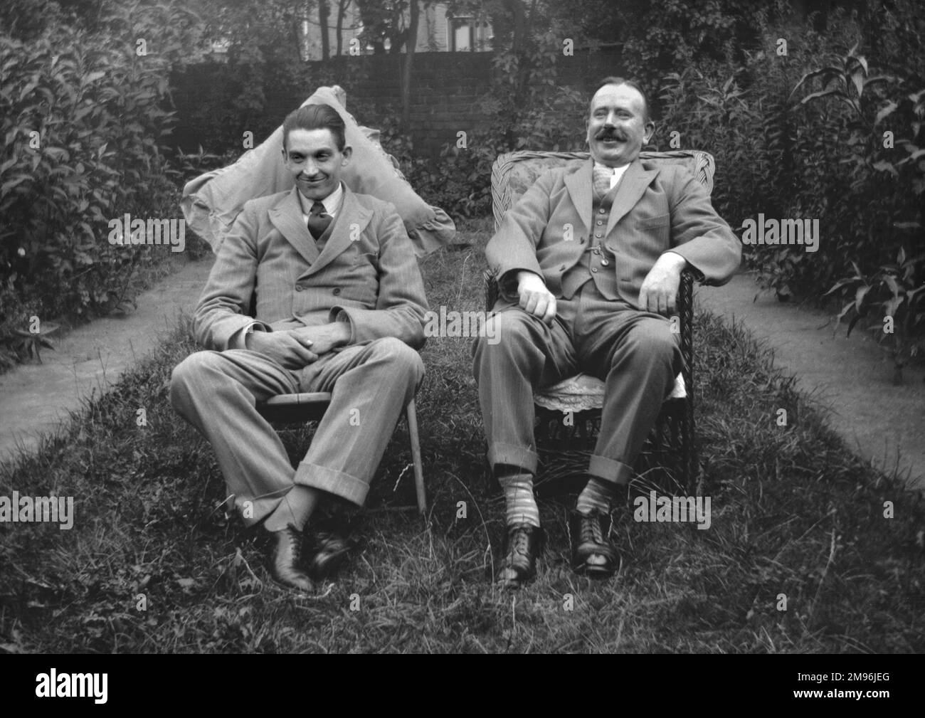 Due uomini seduti in un giardino un po' troppo grande -- il prato ha certamente bisogno di falciare! Foto Stock