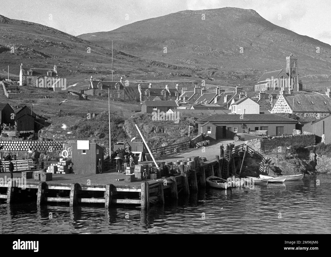Una scena sul mare in Scozia con un molo, case e una chiesa. Barili possono essere visti accumulati su sulla sinistra. Foto Stock