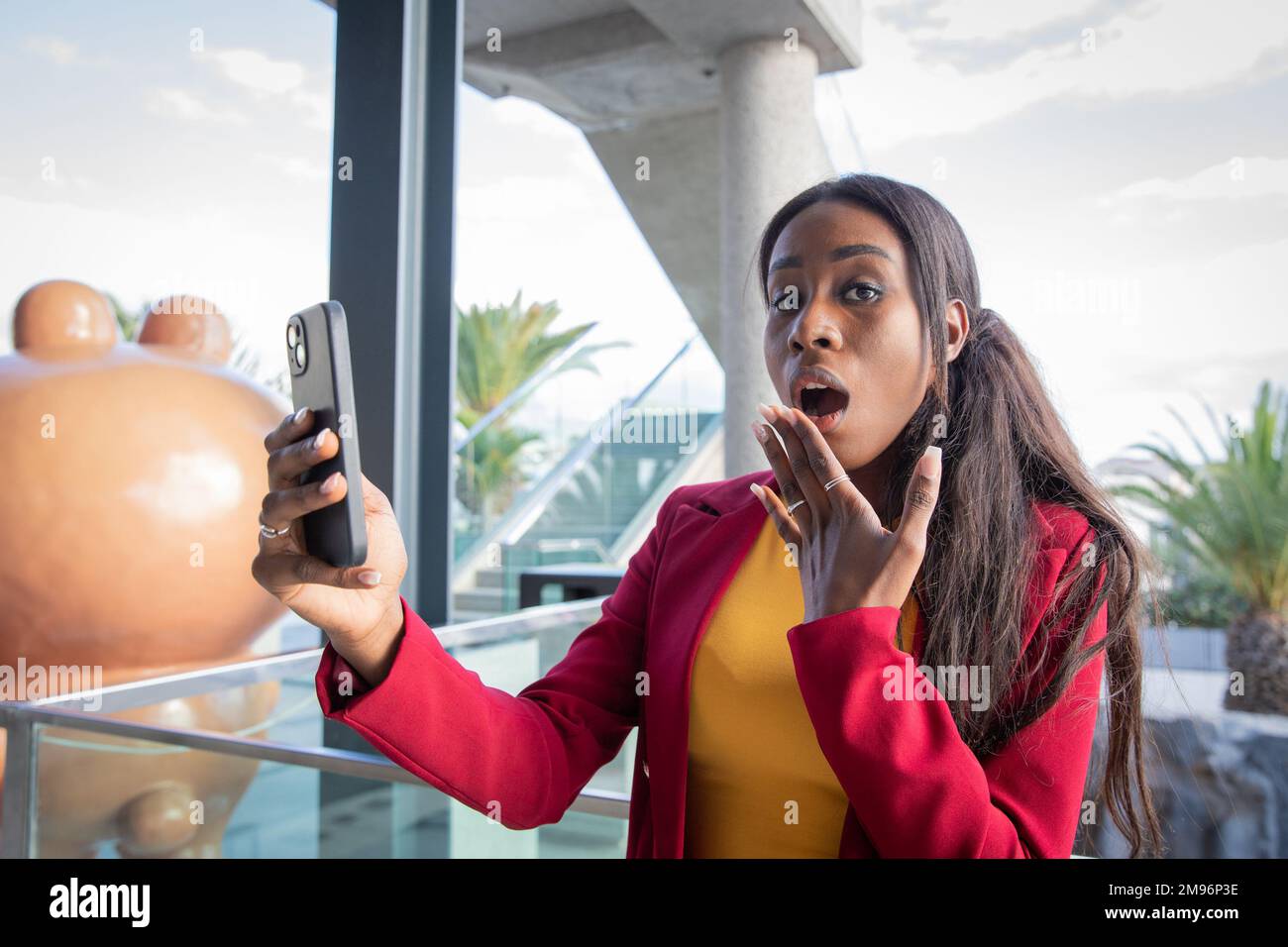 Donna africana con volto sorpreso utilizzando il suo smartphone, donna d'affari al lavoro Foto Stock