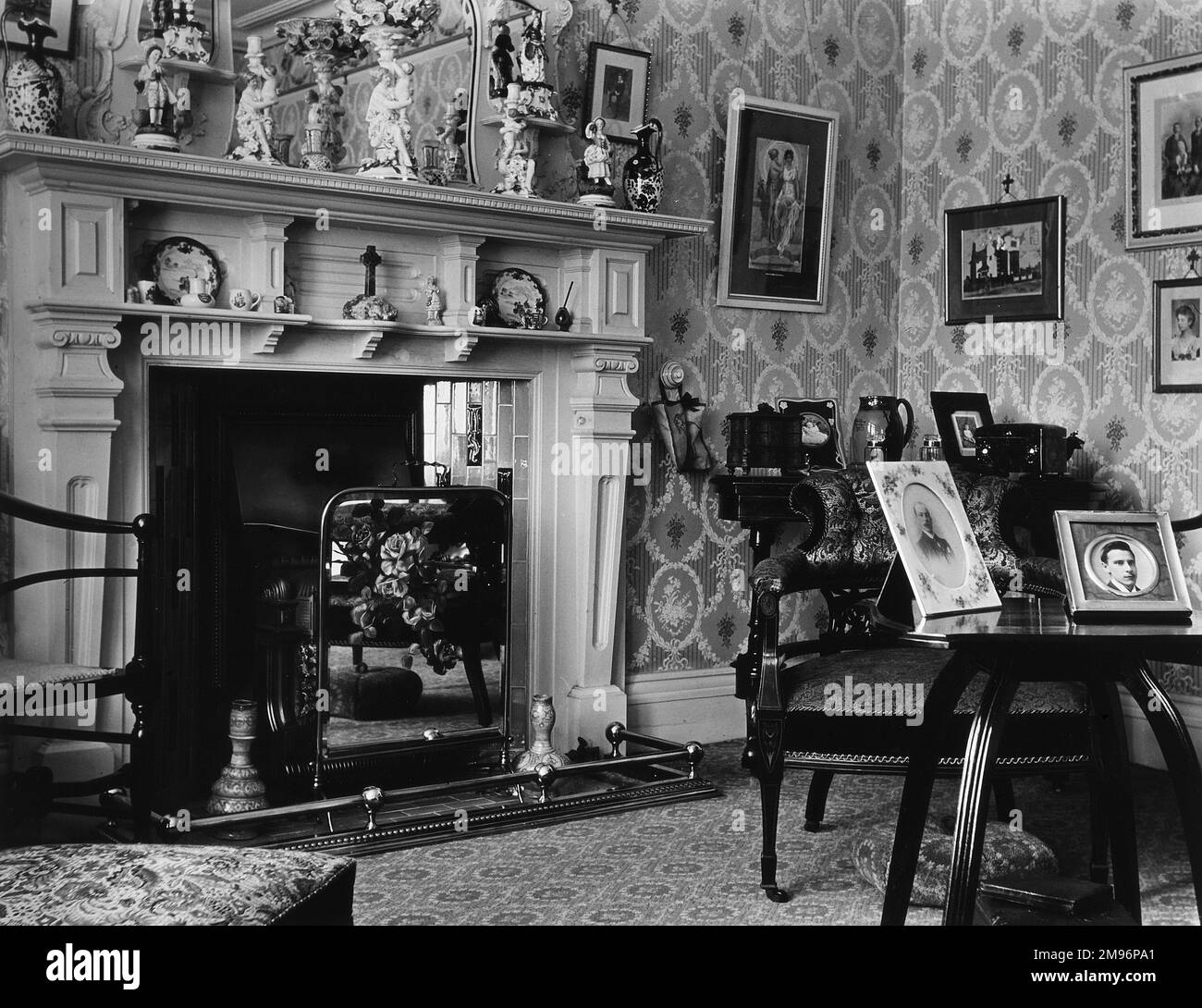 Interno domestico con un grande camino coperto di ornamenti. La carta da parati, il tappeto e le sedie sono tutti modellati, e ci sono diverse immagini sulle pareti e tavoli. Foto Stock