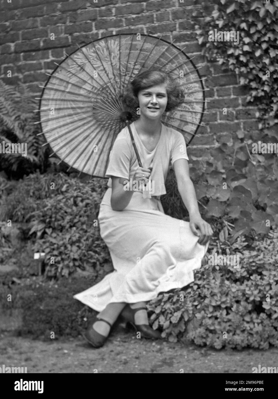 Una giovane donna in giardino con ombrellone. Foto Stock