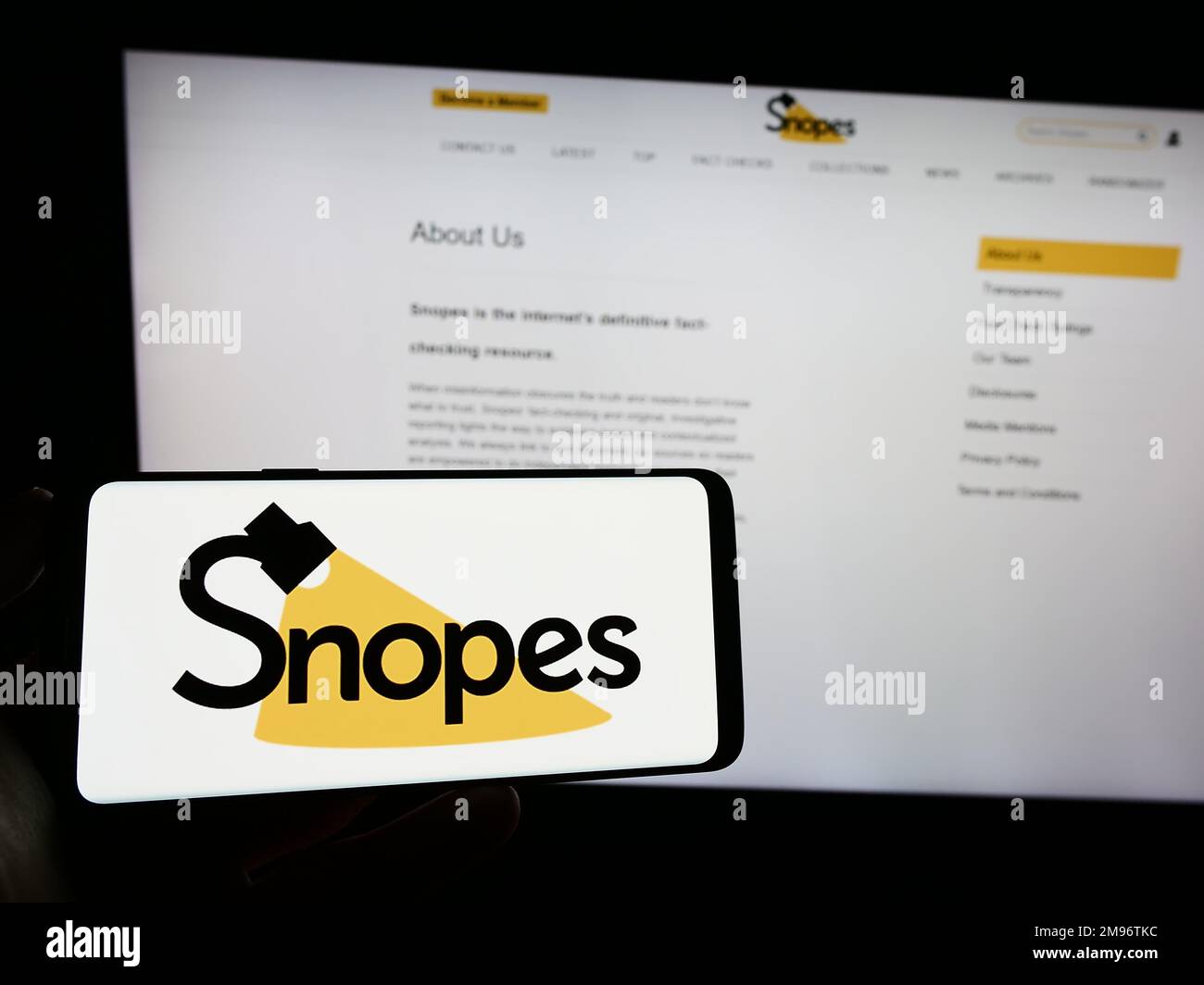 Persona in possesso di smartphone con il logo della piattaforma di controllo dei fatti degli Stati Uniti Snopes Media Group Inc. Sullo schermo di fronte al sito Web. Messa a fuoco sul display del telefono. Foto Stock