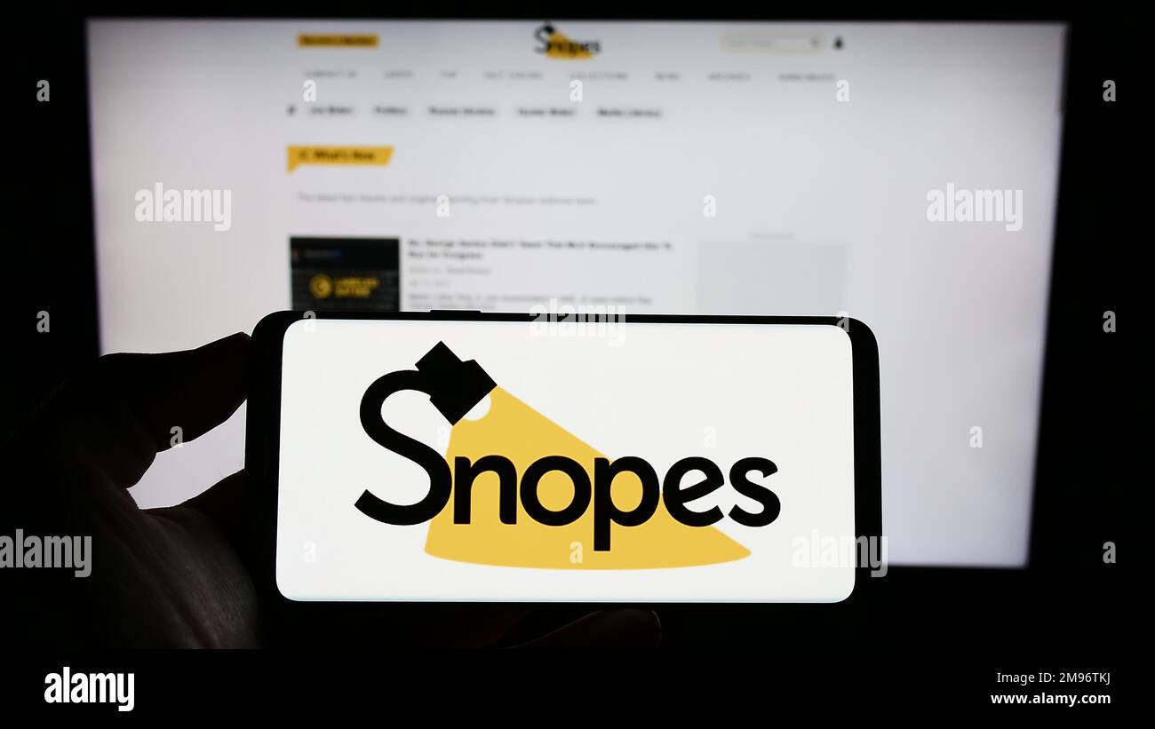 Persona che tiene il telefono mobile con il logo della piattaforma di controllo di fatto degli Stati Uniti Snopes Media Group Inc. Sullo schermo davanti alla pagina web. Messa a fuoco sul display del telefono. Foto Stock