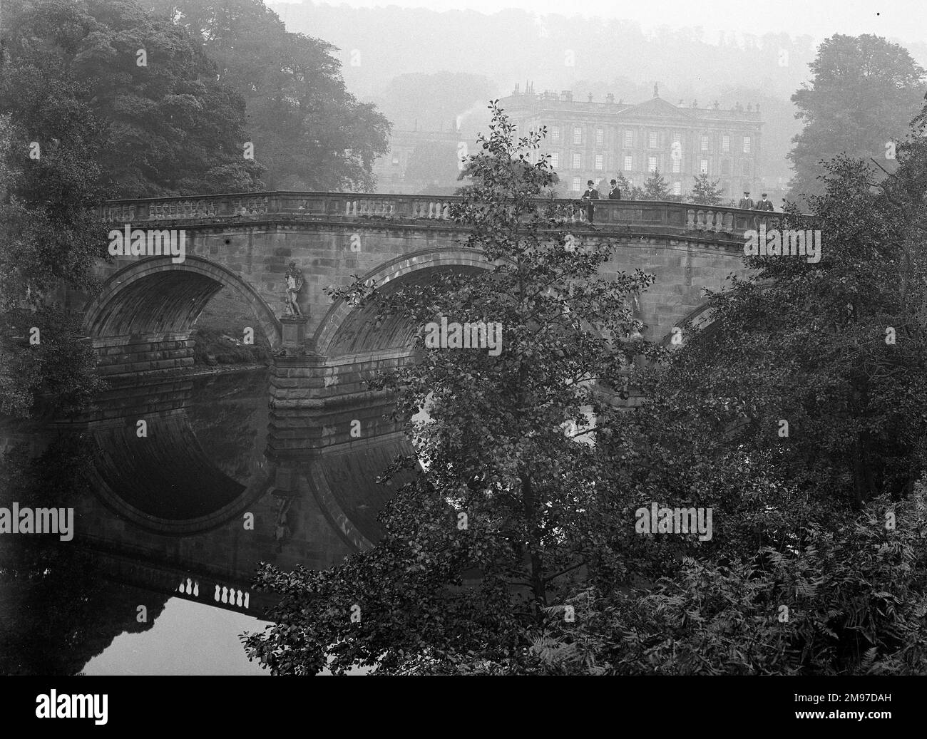 Una splendida fotografia tranquilla, con il ponte riflesso nell'acqua e Chatsworth House nella nebbia sullo sfondo Foto Stock