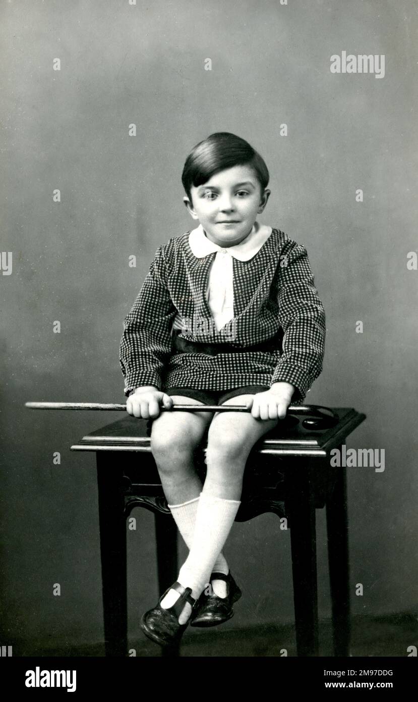 Il ragazzino seduto su uno sgabello, in mano, si posa per la macchina fotografica Foto Stock