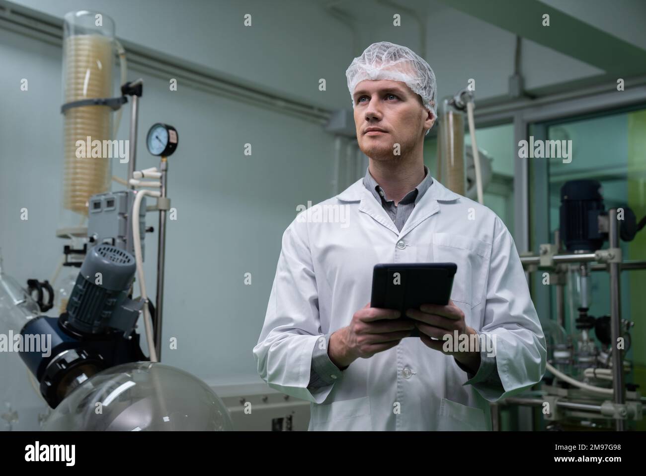 Scienziato maschile, farmacista che lavora in un laboratorio per l'estrazione di cannabis mentre trasporta una compressa contenente dati chimici estratti dalla foglia di canapa Foto Stock