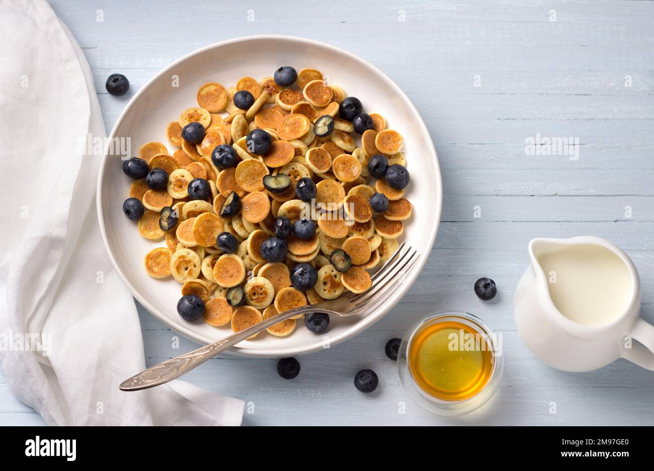 Piatto di Mini Pancakes cereali con crema, miele e frutti di bosco su sfondo azzurro. cibo alla moda. colazione fatta in casa. vista dall'alto. spazio Foto Stock
