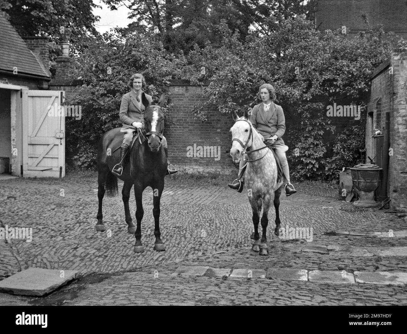 Due giovani donne a cavallo in un cortile stabile. Foto Stock