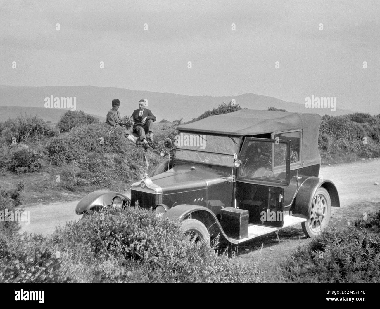 Coppia che si rilassa sul lato di una strada di campagna, con la propria auto parcheggiata in primo piano. Foto Stock