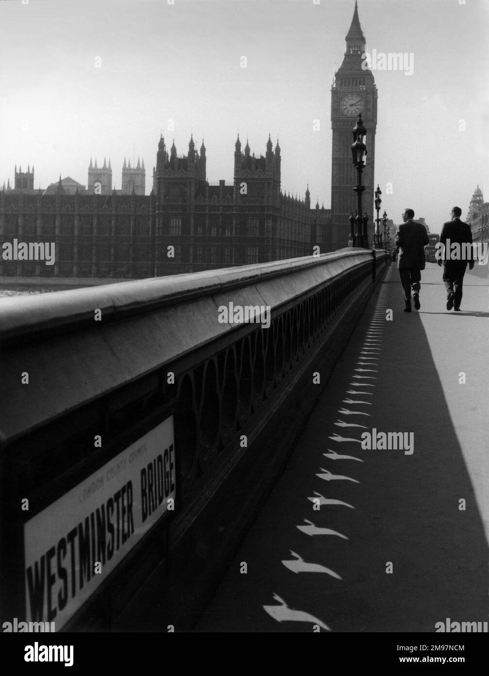 Due uomini che camminano sul ponte di Westminster con le Camere del Parlamento come sfondo. Foto Stock