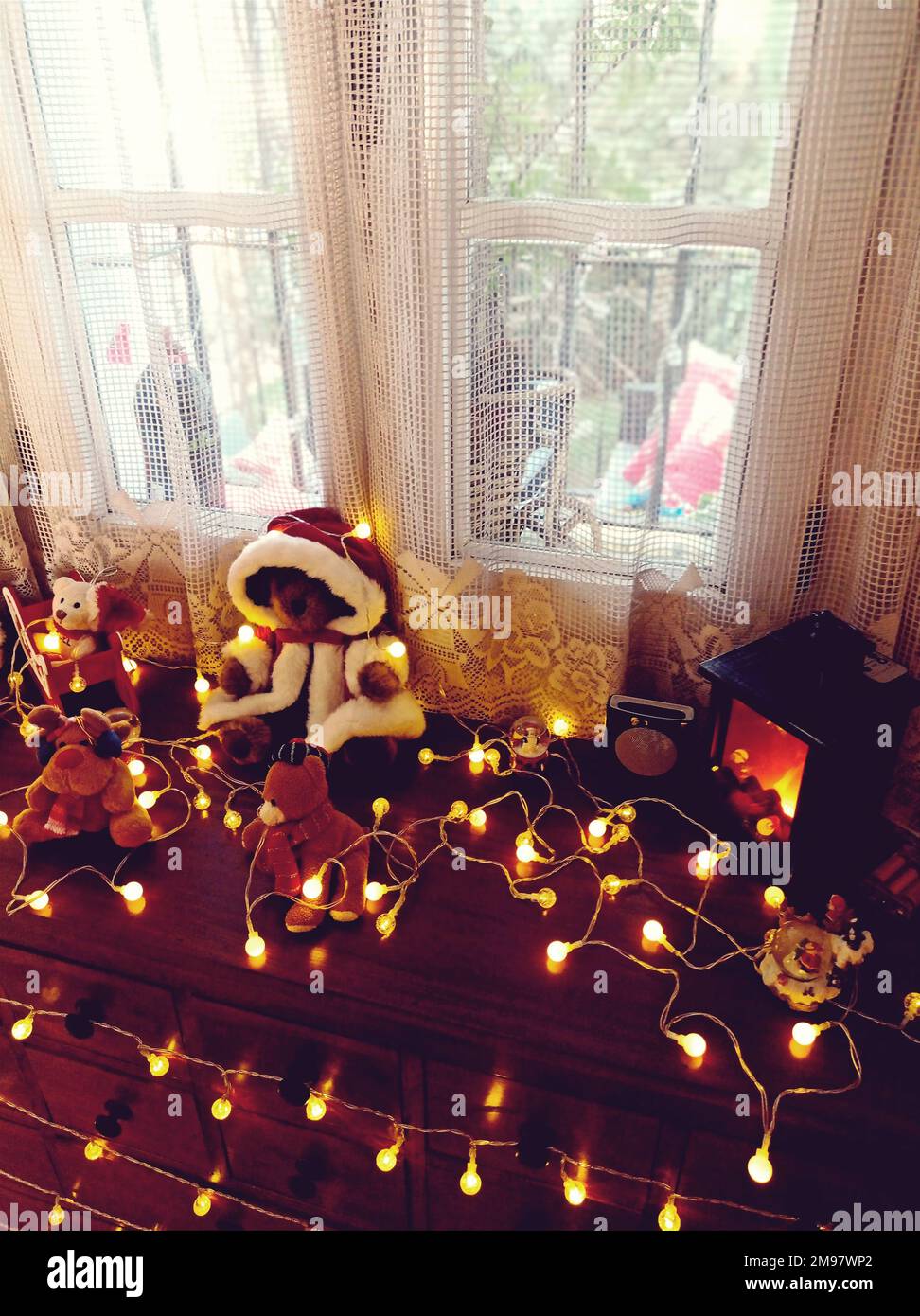Primo piano di decorazioni natalizie assortite e luci a corda su un comò vicino a una finestra Foto Stock
