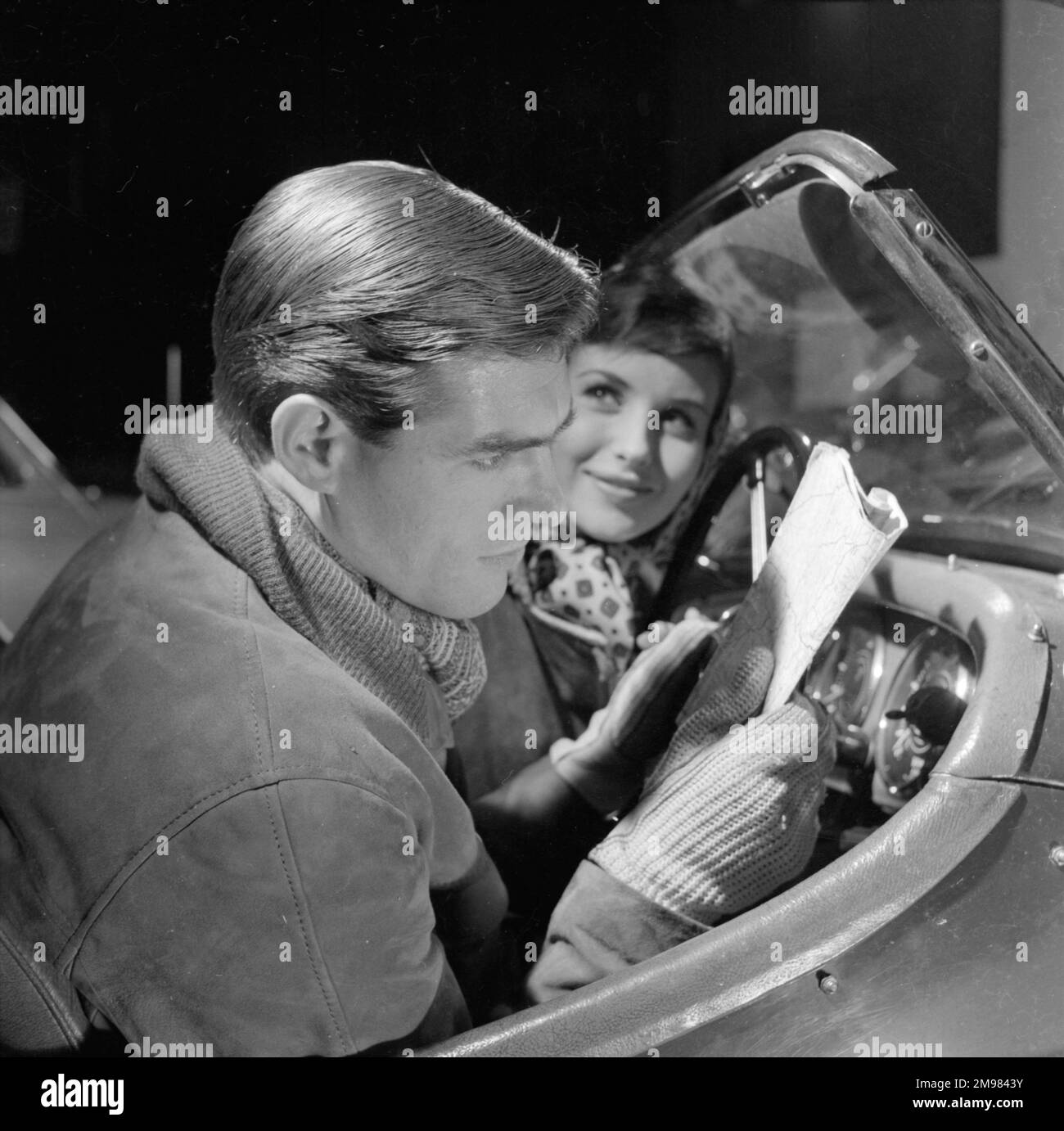 Pubblicità per i prodotti per capelli Silvikrin -- modelli maschili e femminili (Peter Christian e Anne Cave) in una scena di rally auto. Foto Stock