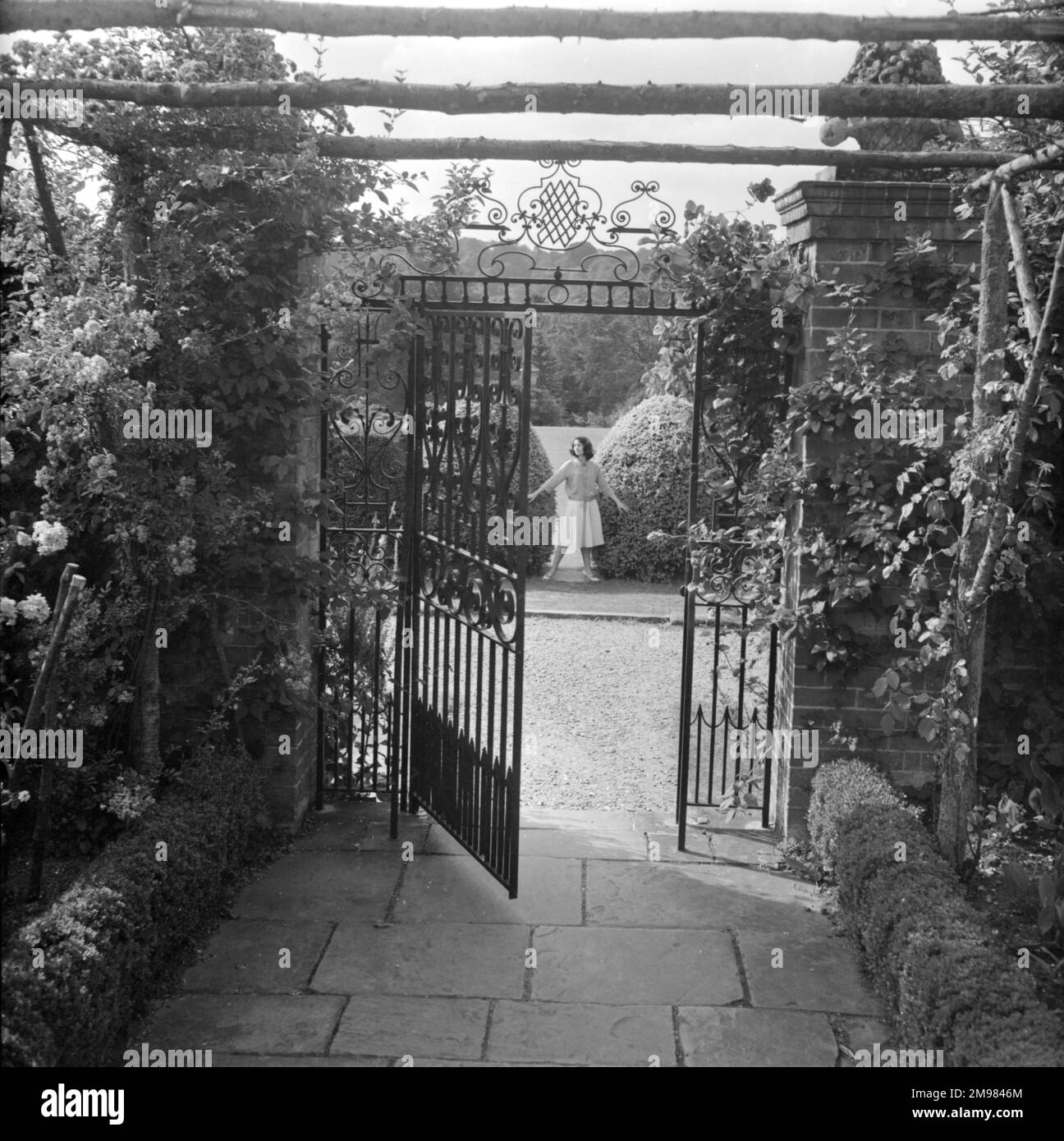 Cancello in ferro battuto in giardino con modello femminile in lontananza. Foto Stock