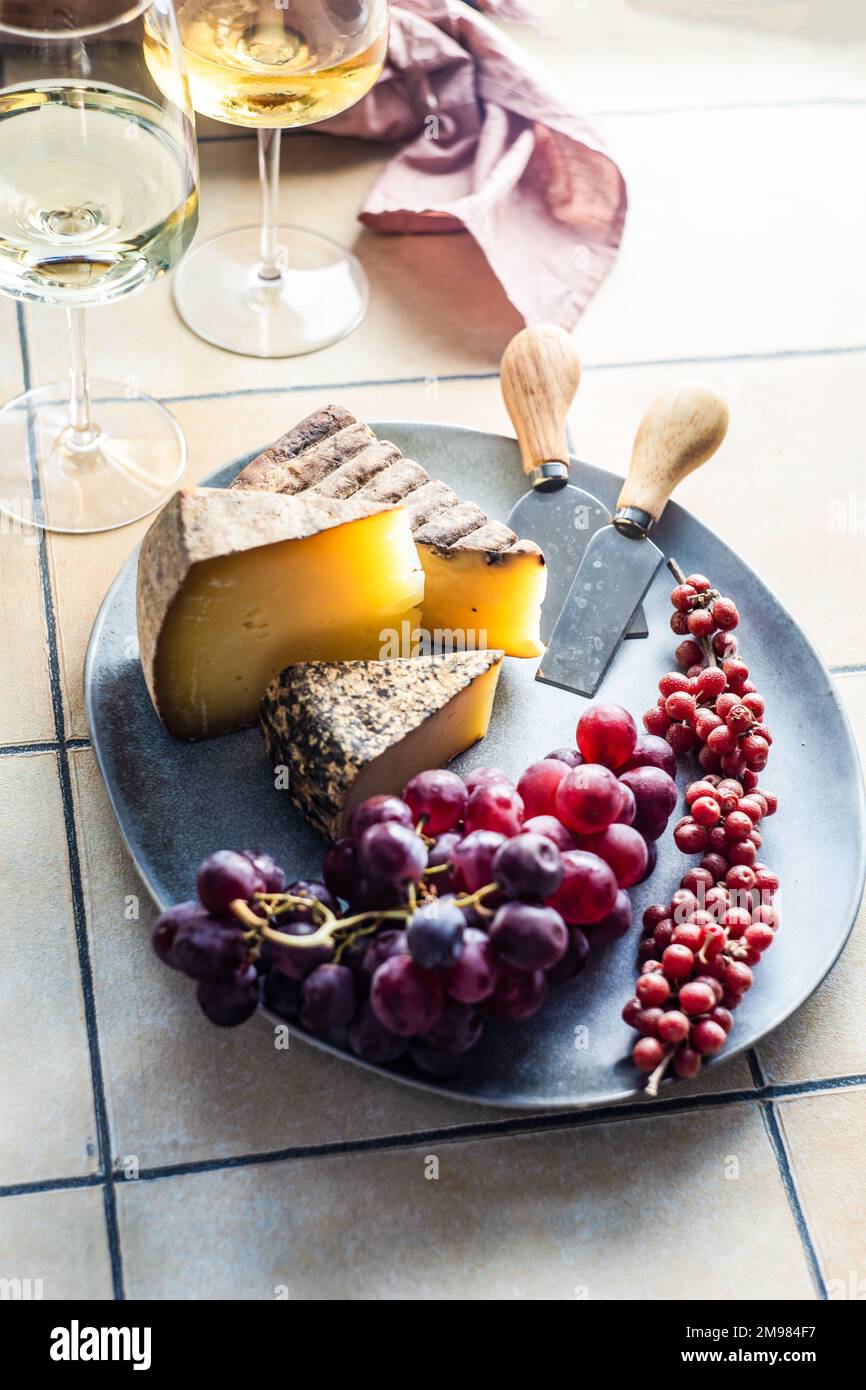 Primo piano di formaggi, barbacca e piatto d'uva con due bicchieri di vino bianco Foto Stock