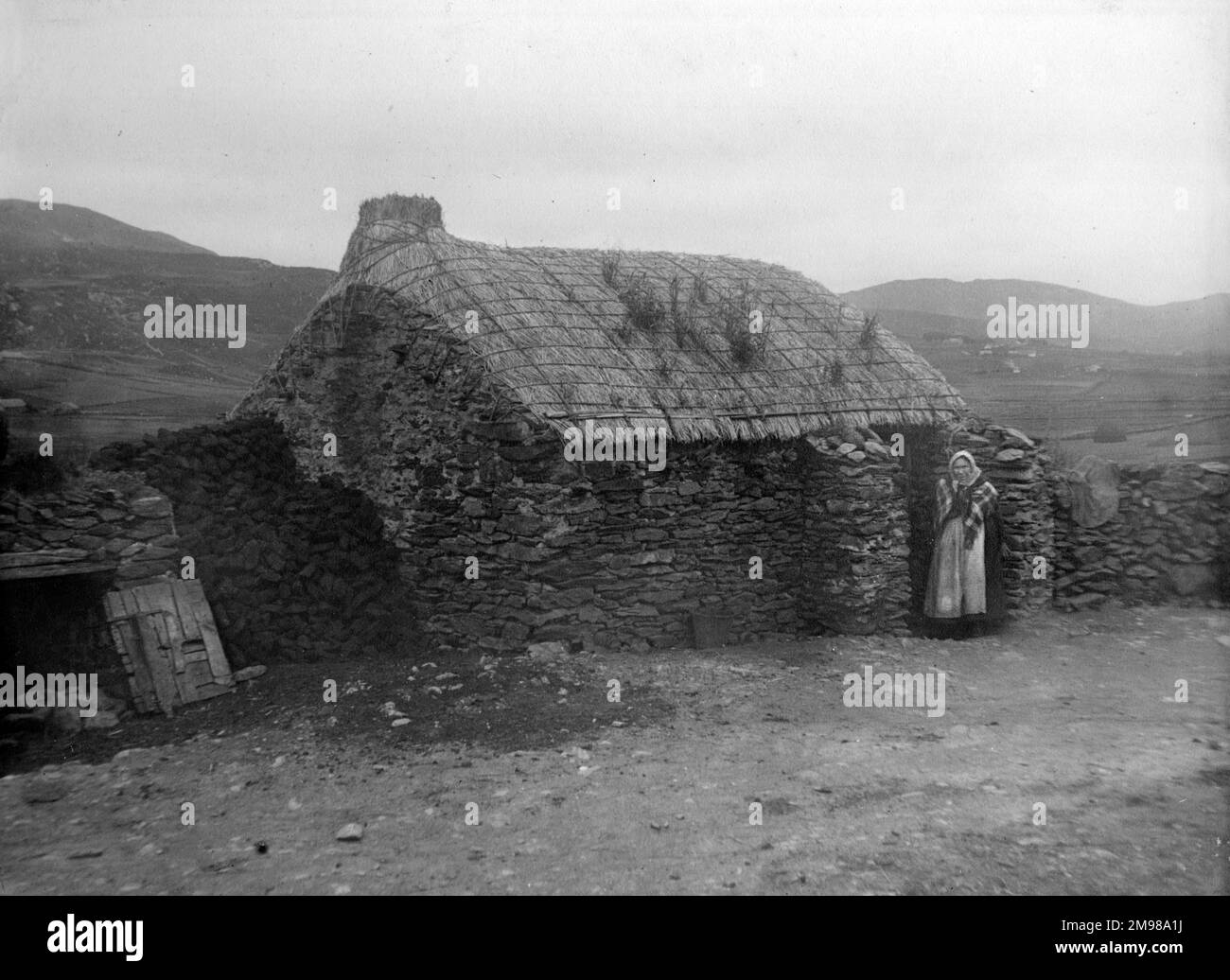 Cottage con una camera singola con una donna in piedi alla porta in Glen Columbkille (Glencolmcille, Gleann Cholm Cille), County Donegal, Irlanda nord-occidentale. Foto Stock
