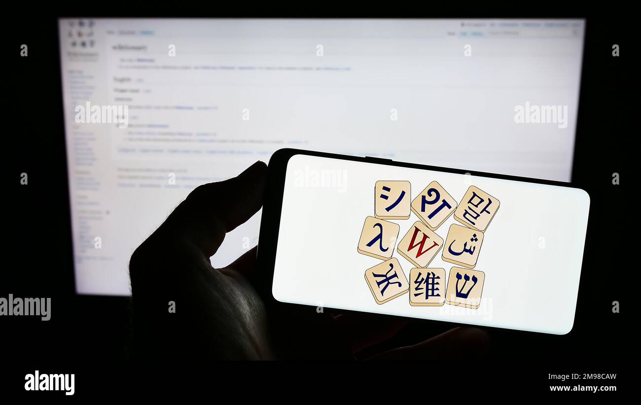 Persona che tiene lo smartphone con il logo del dizionario online Wiktionary (Wikimedia) sullo schermo di fronte al sito web. Messa a fuoco sul display del telefono. Foto Stock