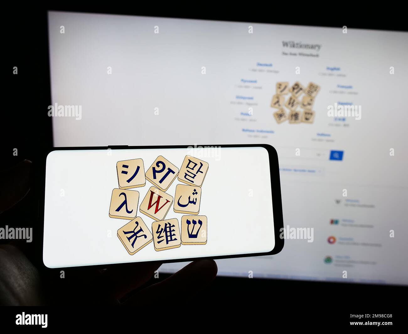 Persona che tiene il telefono cellulare con il logo del dizionario online Wiktionary (Wikimedia) sullo schermo di fronte alla pagina web. Messa a fuoco sul display del telefono. Foto Stock